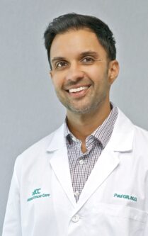 Head-and-shoulders portrait of Dr. Paul Gill, M.D., in a white lab coat, smiling at the camera. 